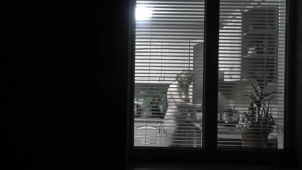 Peeping. Voyeur. Neighbor pervert voyeur in evening on street looks out window as naked sexy neighbor in kitchen prepares dinner for her husband. Naked in public. Naked at home. Family.  Outdoor videos